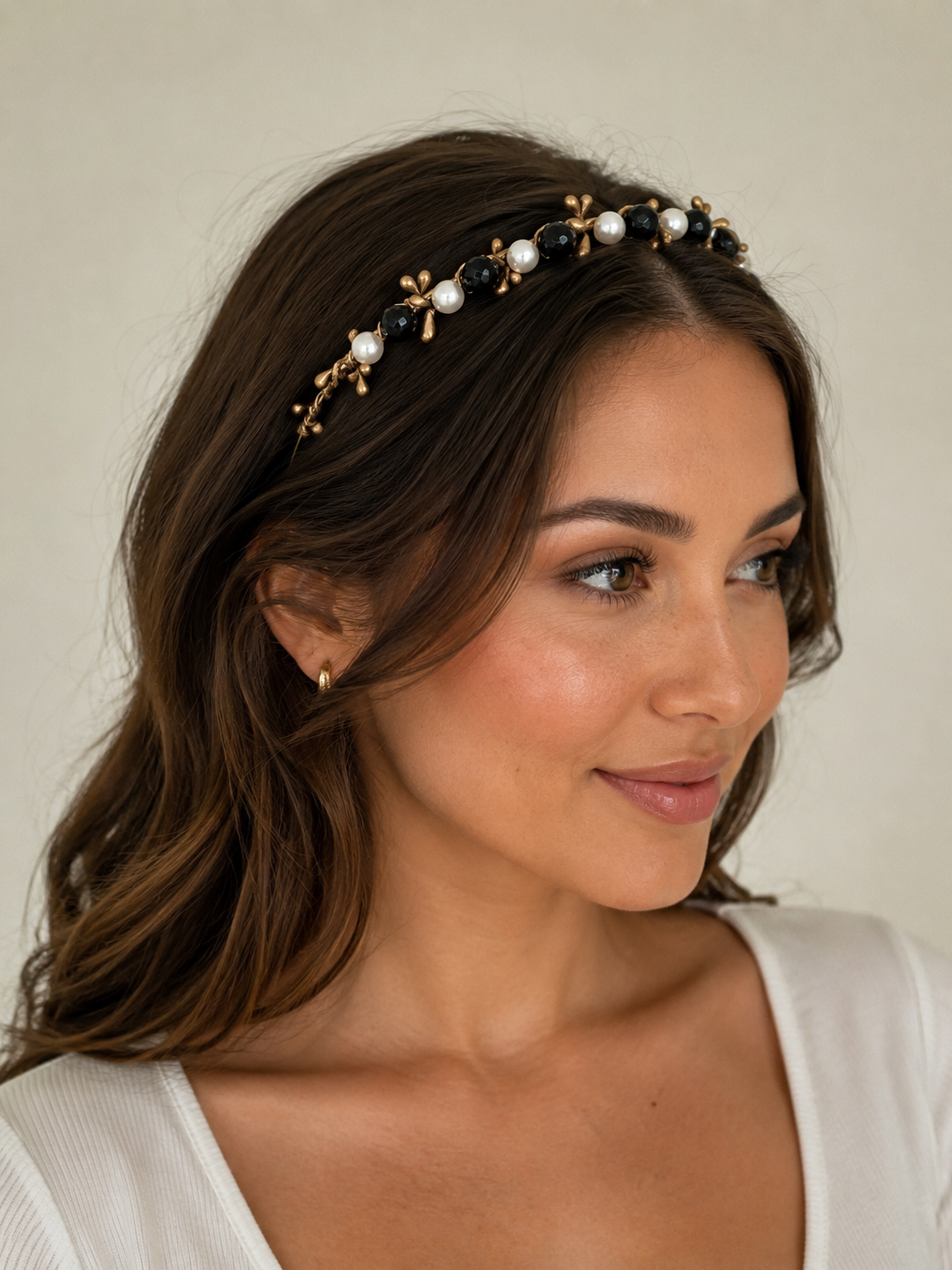 Woman wearing a decorative headband with pearls and black stones on a neutral background