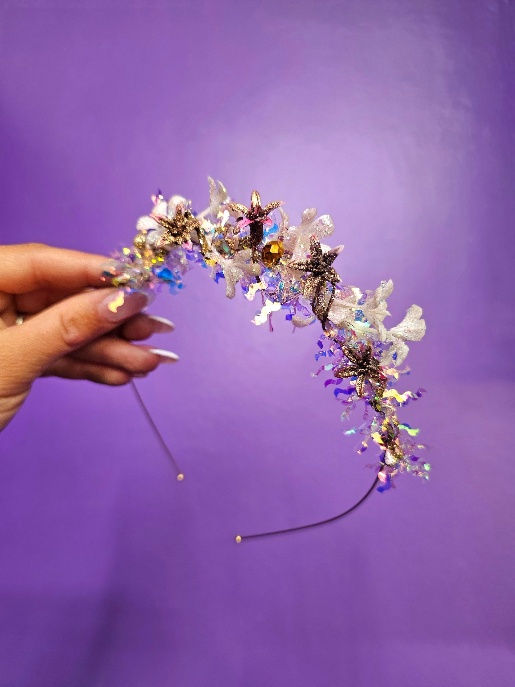 Decorative headband with flowers and beads held by a hand against a purple background