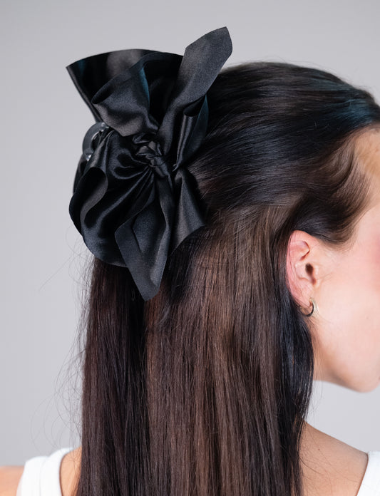 Model wearing an oversized black satin hair bow clip in a half-up hairstyle